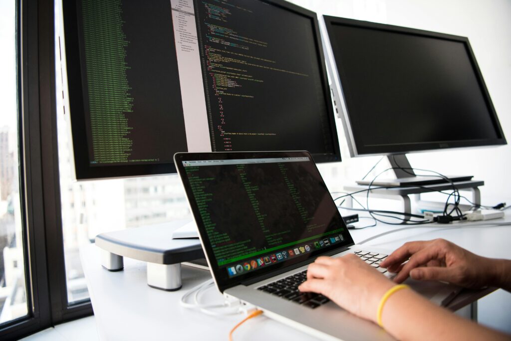 African software developer coding at a desk with multiple screens displaying data and code.